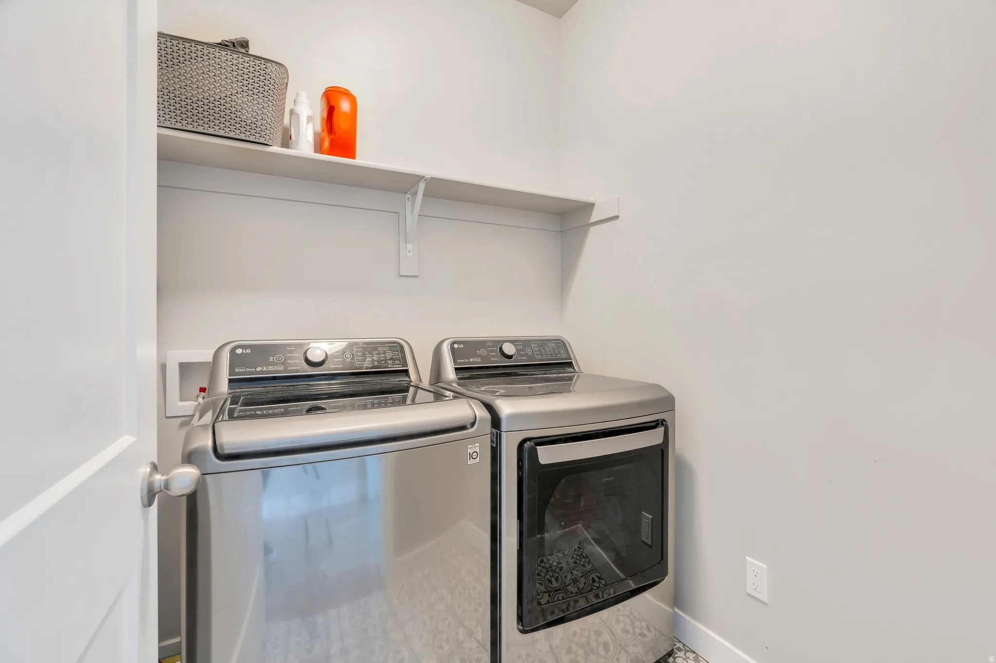 Dedicated utility area featuring a wall-mounted shelving unit, contemporary white walls, and a durable tile flooring