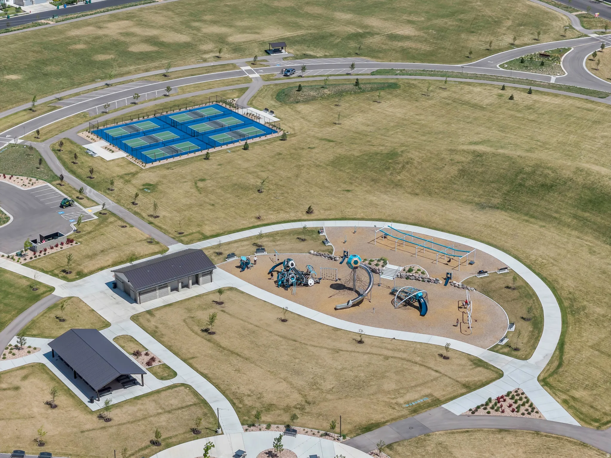 Expansive recreational area featuring multiple tennis courts, a large playground, a covered picnic pavilion, and a community building