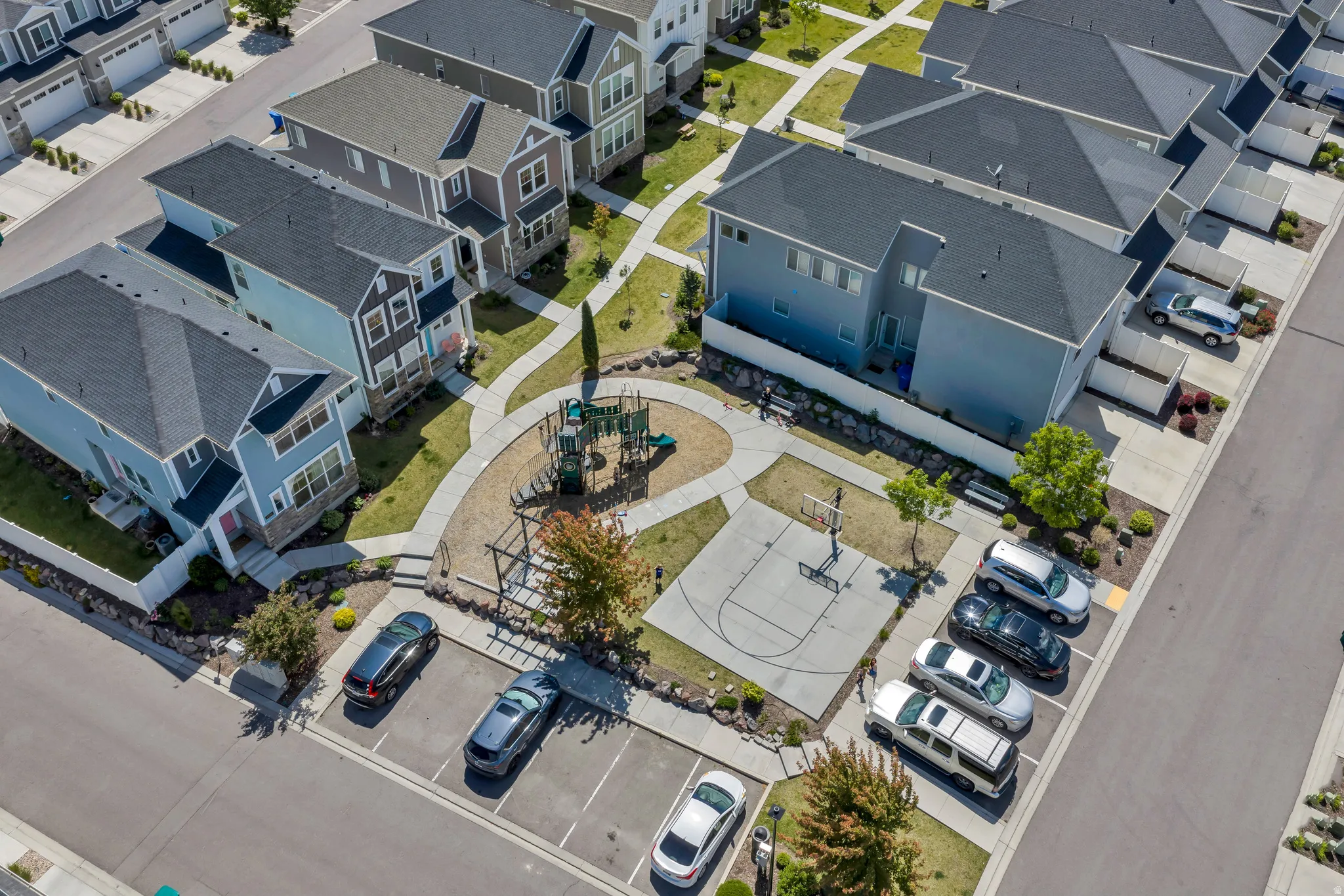 Community park area featuring a playground, basketball court, paved pathways, and mature landscaping