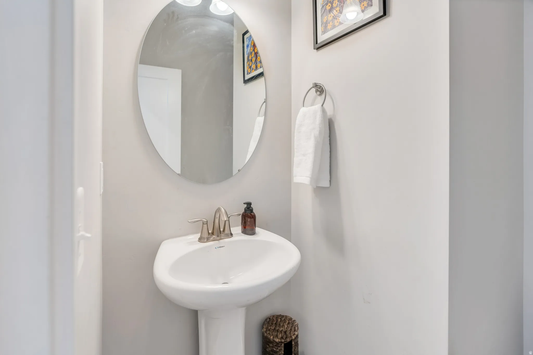 Pedestal sink with brushed nickel faucet, oval mirror, and wall-mounted towel ring