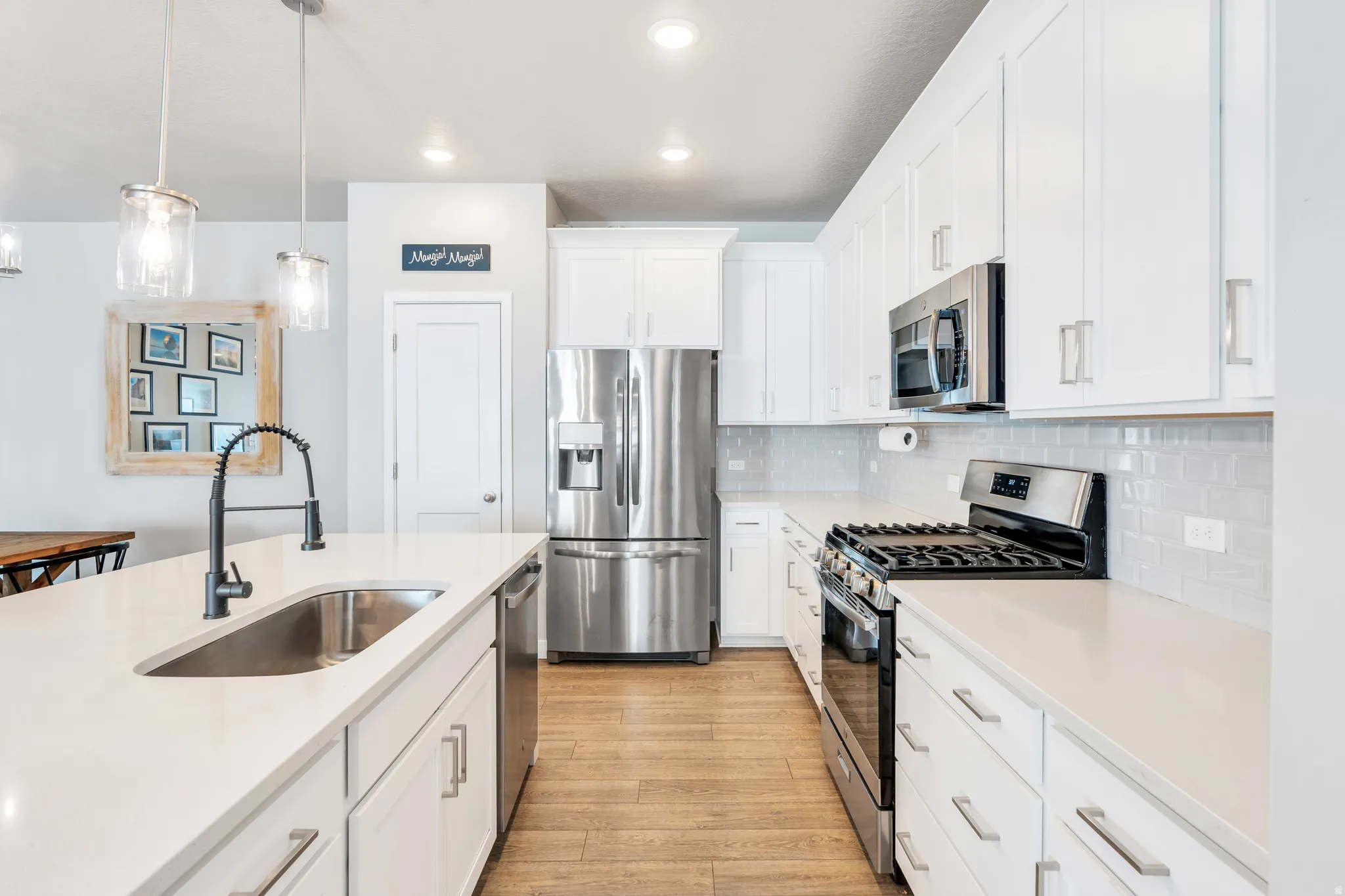 Modern kitchen featuring white cabinetry, stainless steel appliances, light gray subway tile backsplash, light wood-finish flooring, and a kitchen island with an undermount sink and matte black faucet
