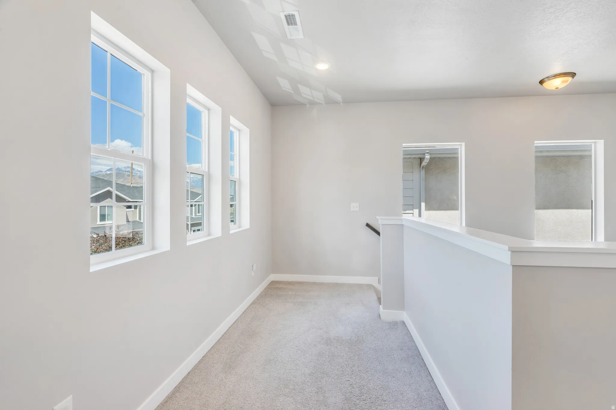 Upper landing featuring three vertical windows, neutral wall tones, light gray carpet, recessed lighting, and a white half-wall railing