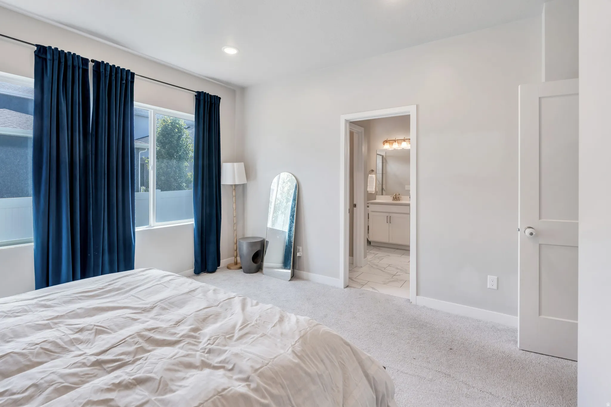 Carpeted room with light gray walls, an open doorway to a bathroom with a vanity, and a separate white paneled door