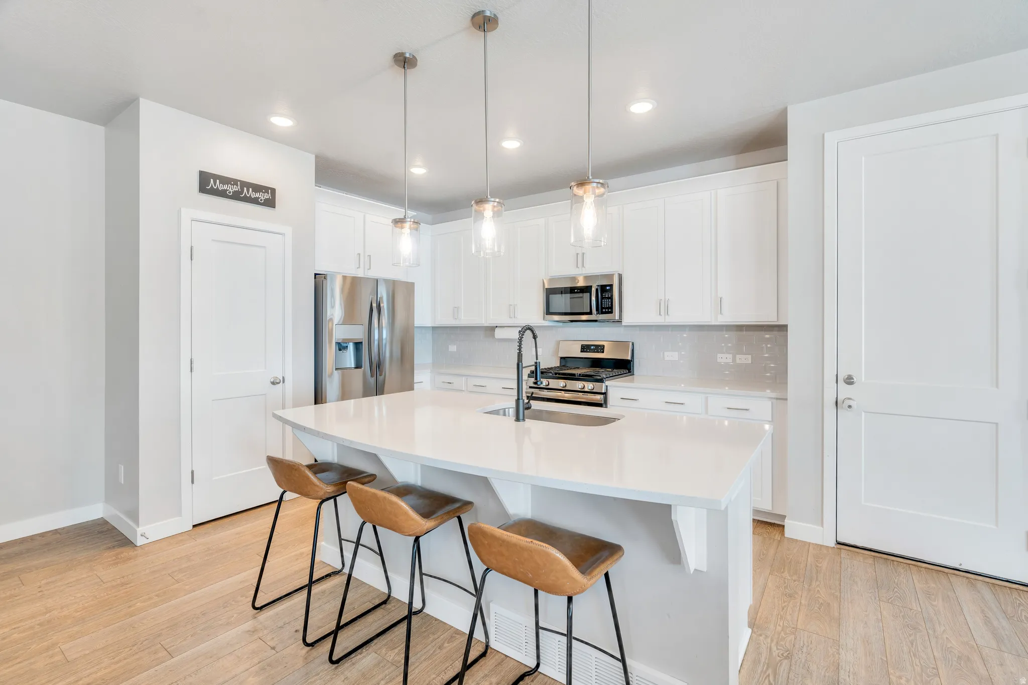 Modern kitchen featuring a large central island with countertop seating, stainless steel appliances, white cabinetry, and wood-finish flooring