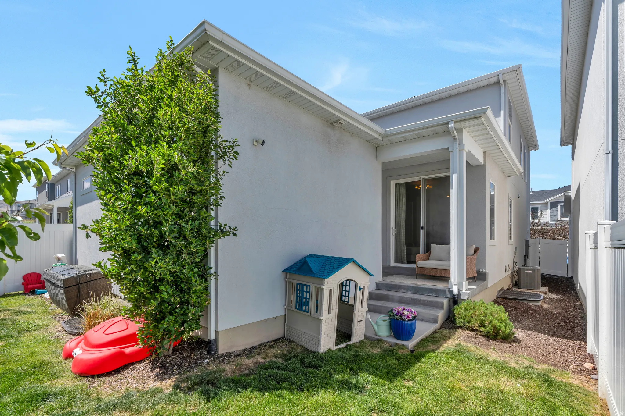 Manicured lawn area featuring a mature tree, a privacy fence, and a concrete patio with sliding glass door access