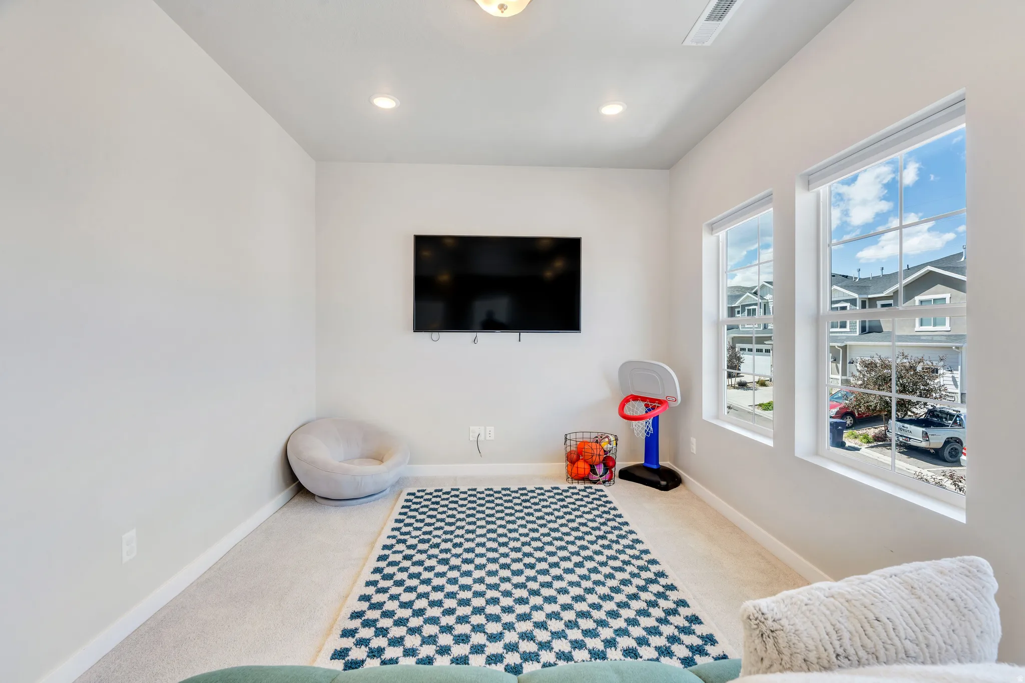 Versatile room featuring two large windows, recessed lighting, wall-mounted television, and light-toned carpeting
