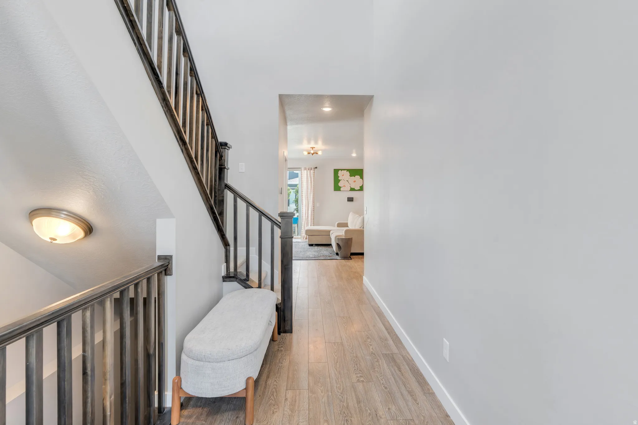 Contemporary interior hallway featuring wood-finish flooring, light grey walls, and a staircase with dark wood-finish railings