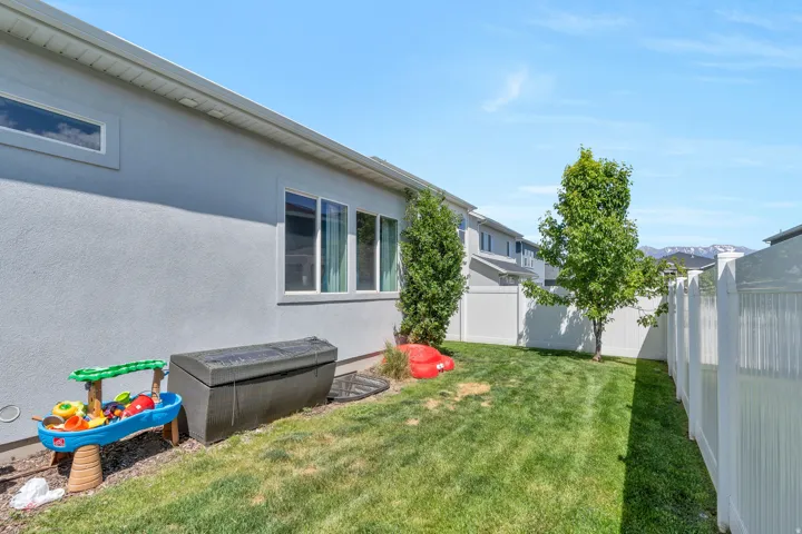 Fenced backyard featuring a manicured lawn, established trees, and white vinyl perimeter fencing