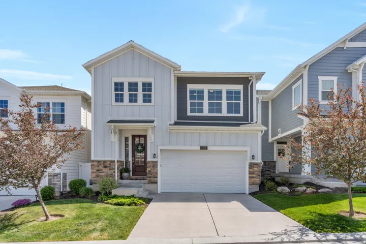 Contemporary multi-story residence featuring light and dark siding accents, a two-car garage, stone facade details, a covered entry, and a manicured lawn with mature landscaping