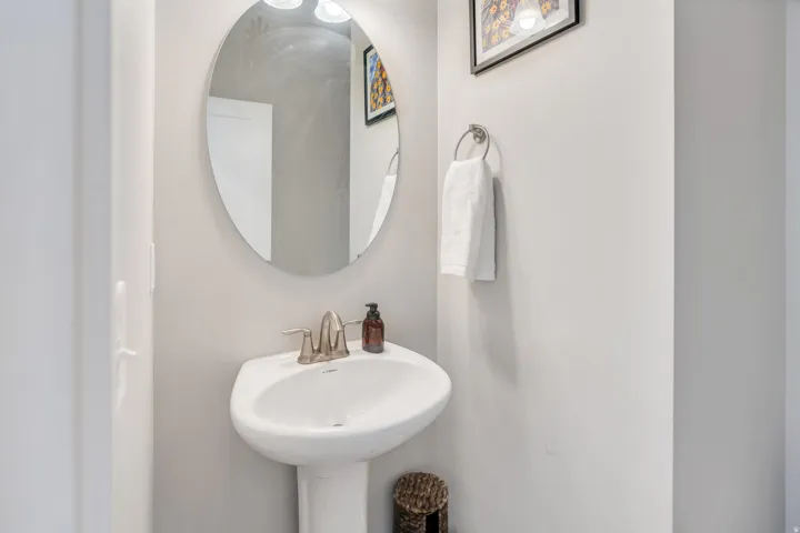 Pedestal sink with brushed nickel faucet, oval mirror, and wall-mounted towel ring