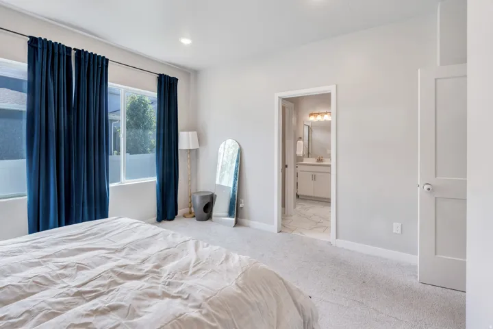 Carpeted room with light gray walls, an open doorway to a bathroom with a vanity, and a separate white paneled door