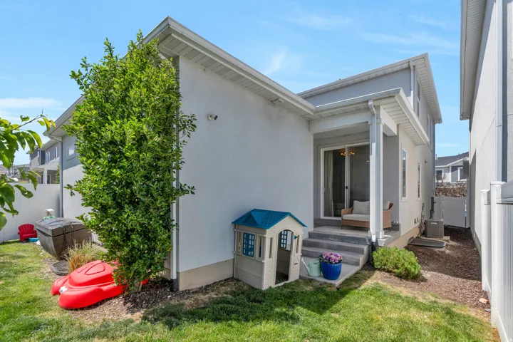 Manicured lawn area featuring a mature tree, a privacy fence, and a concrete patio with sliding glass door access