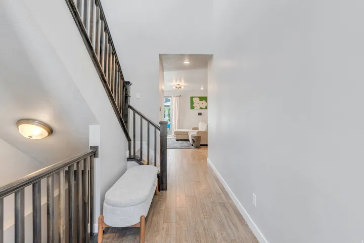Contemporary interior hallway featuring wood-finish flooring, light grey walls, and a staircase with dark wood-finish railings