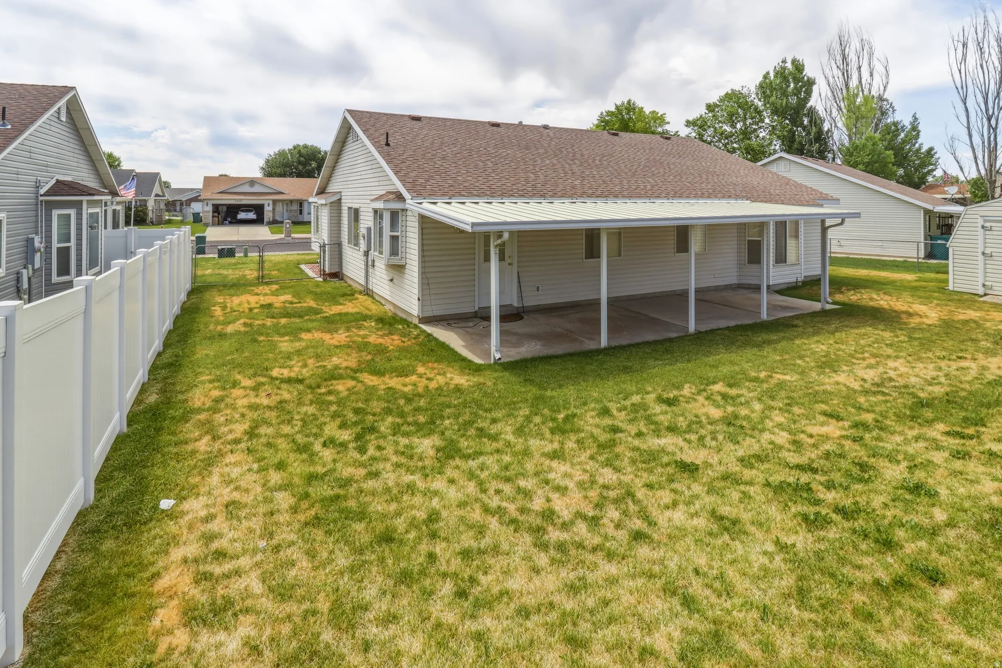 Expansive backyard featuring a covered patio, vinyl siding, a brown shingle roof, and a white privacy fence