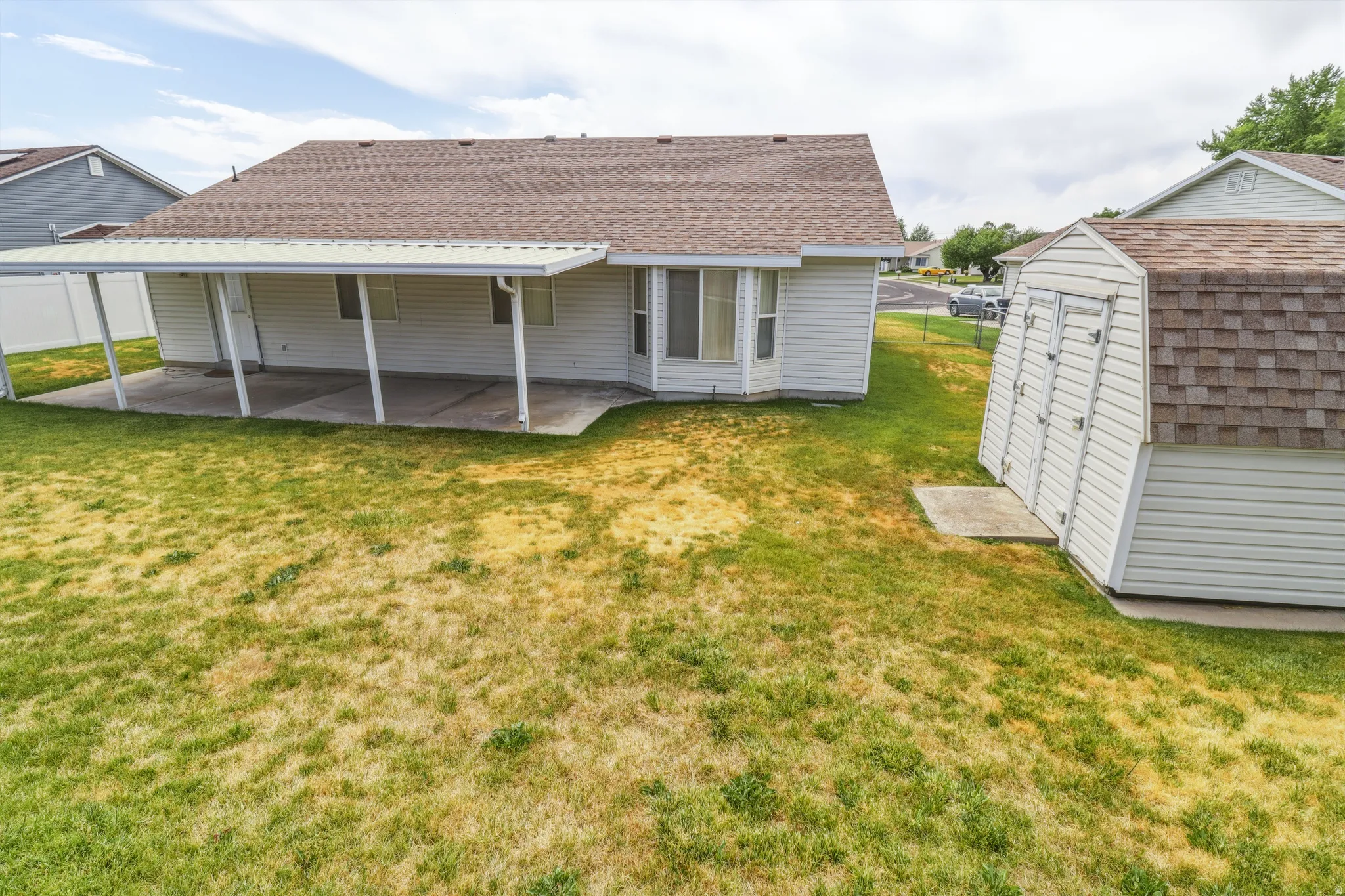 Rear exterior featuring a covered patio, concrete slab, and a separate storage shed with shingle roofing