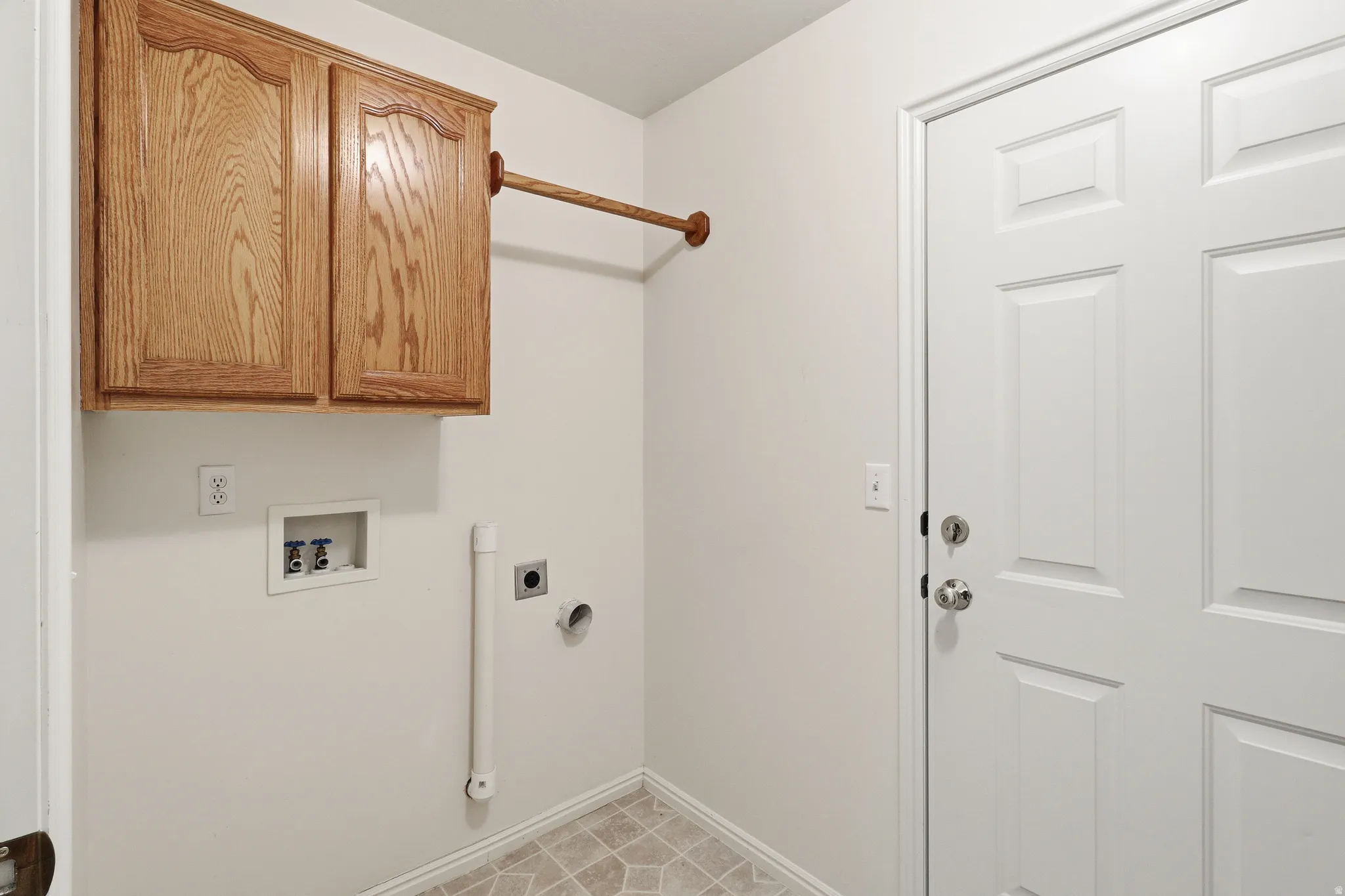 Dedicated laundry area featuring oak-finish cabinetry with a hanging rod, utility hookups, and light-toned flooring