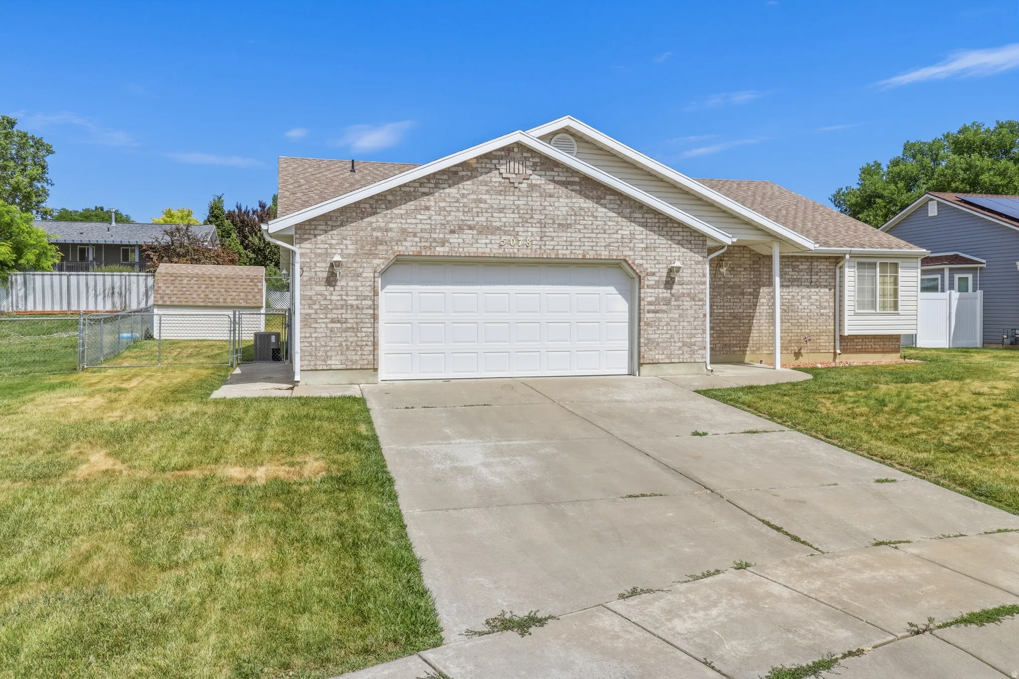 Brick facade residence featuring an attached two-car garage, concrete driveway, and a separate storage shed