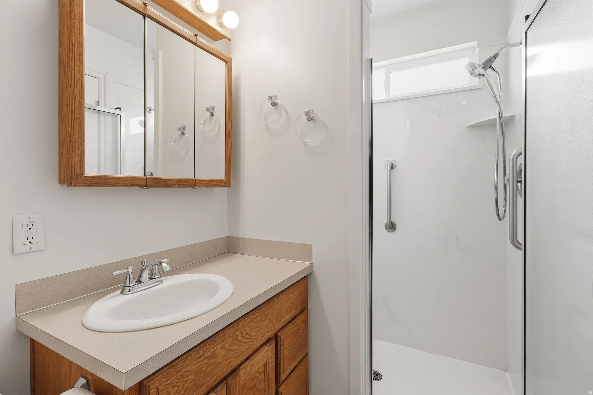 Bathroom vanity with a wood-finish cabinet, integrated sink, chrome faucet, and overhead mirrored medicine cabinet