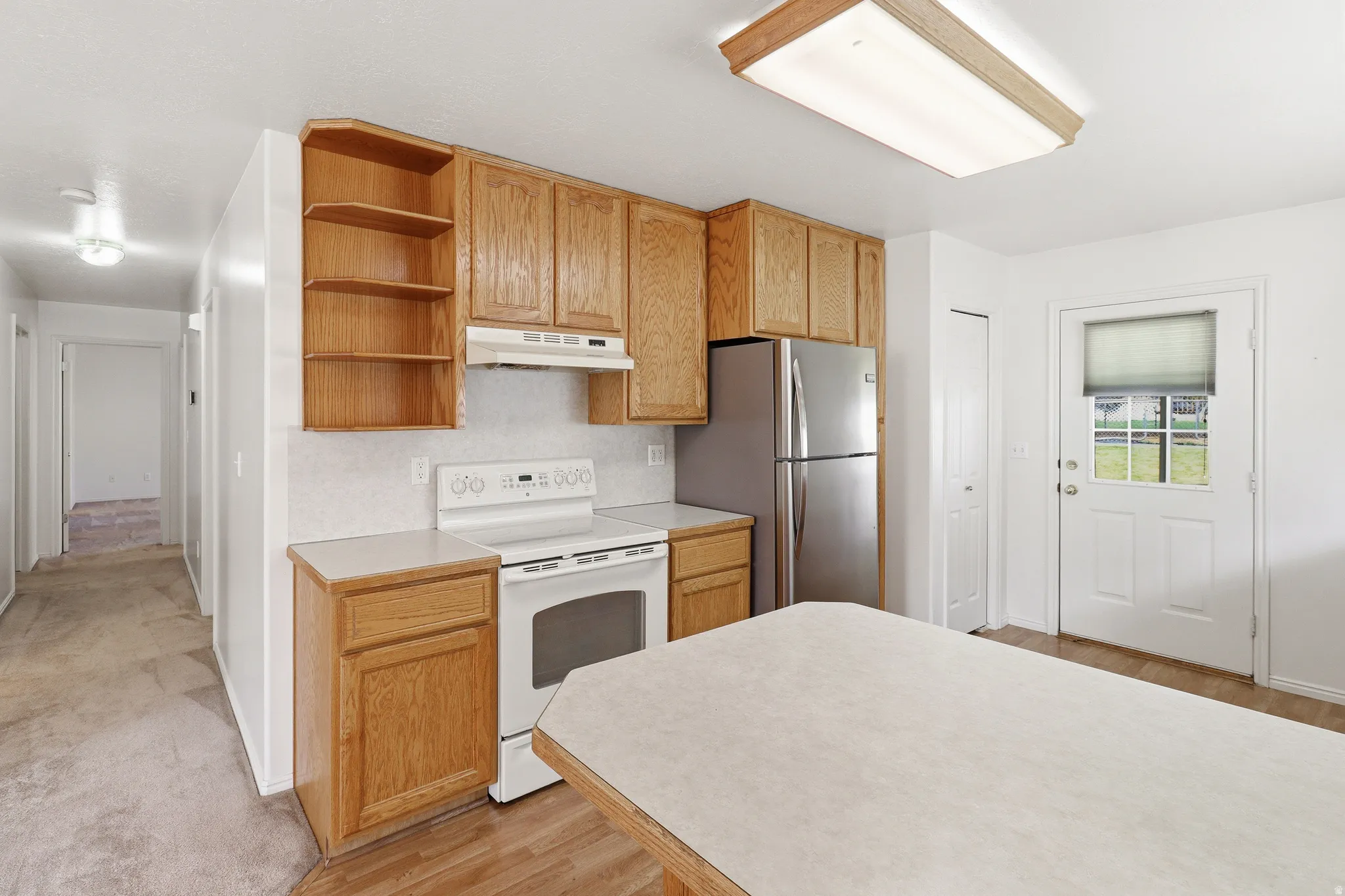 Kitchen featuring wood cabinetry, white appliances, a stainless steel refrigerator, and a light-colored countertop
