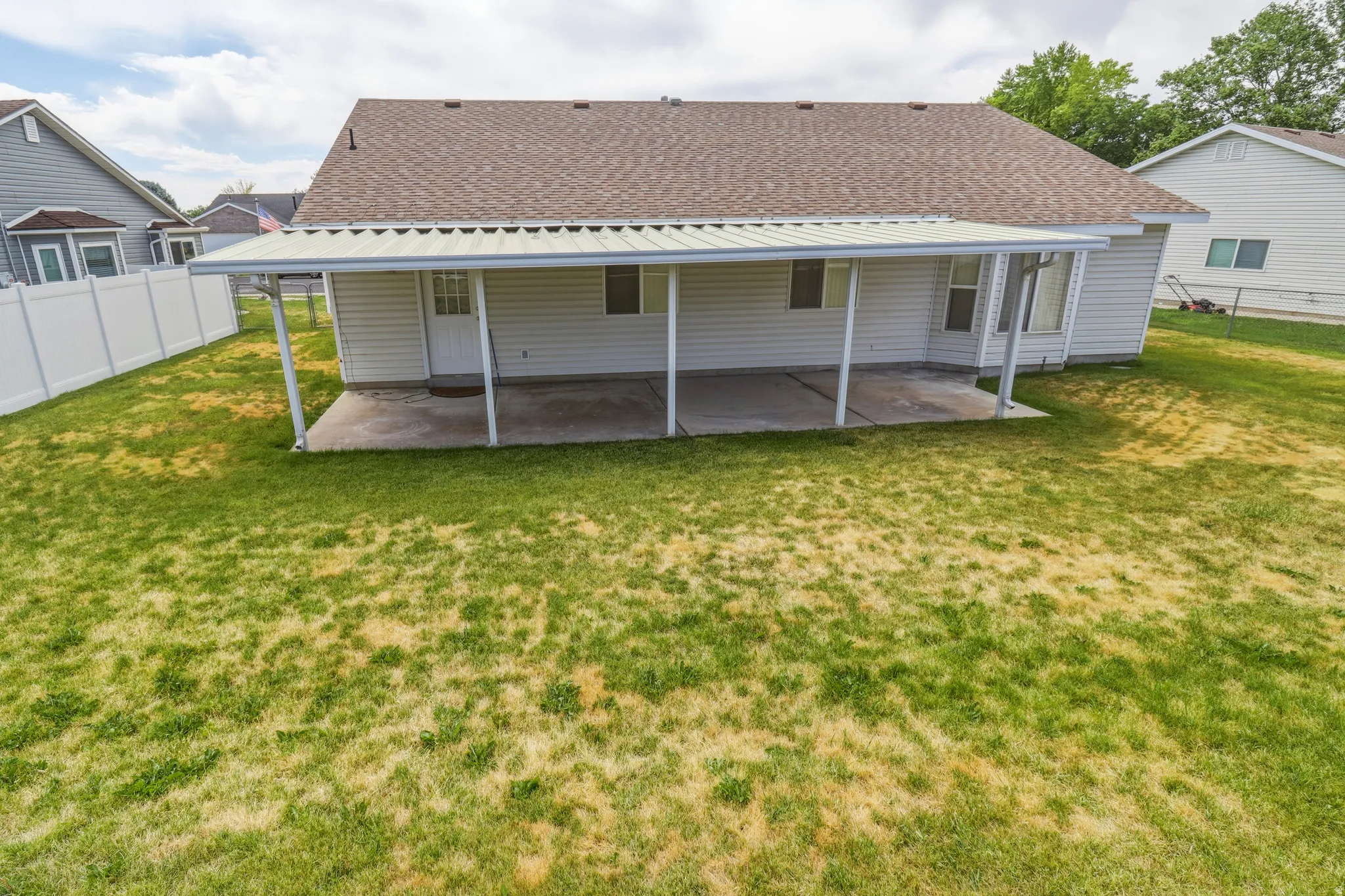 Expansive backyard featuring a covered patio, white vinyl fencing, and a shingled roof