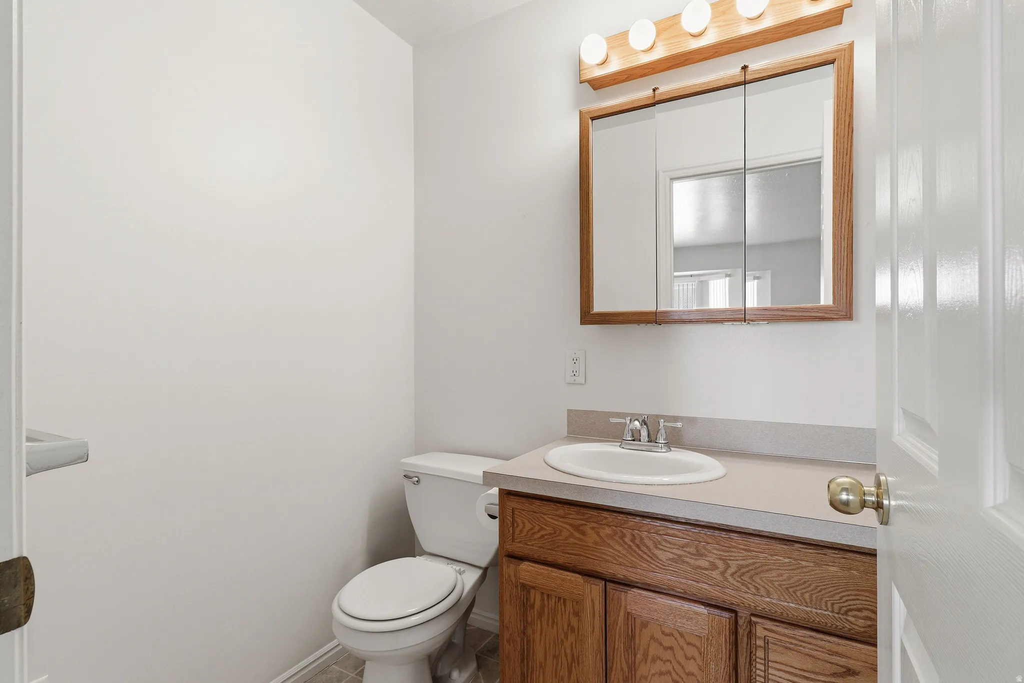 Bathroom featuring a white toilet, wood-finish vanity with a light-colored countertop, and an oval sink with a chrome faucet