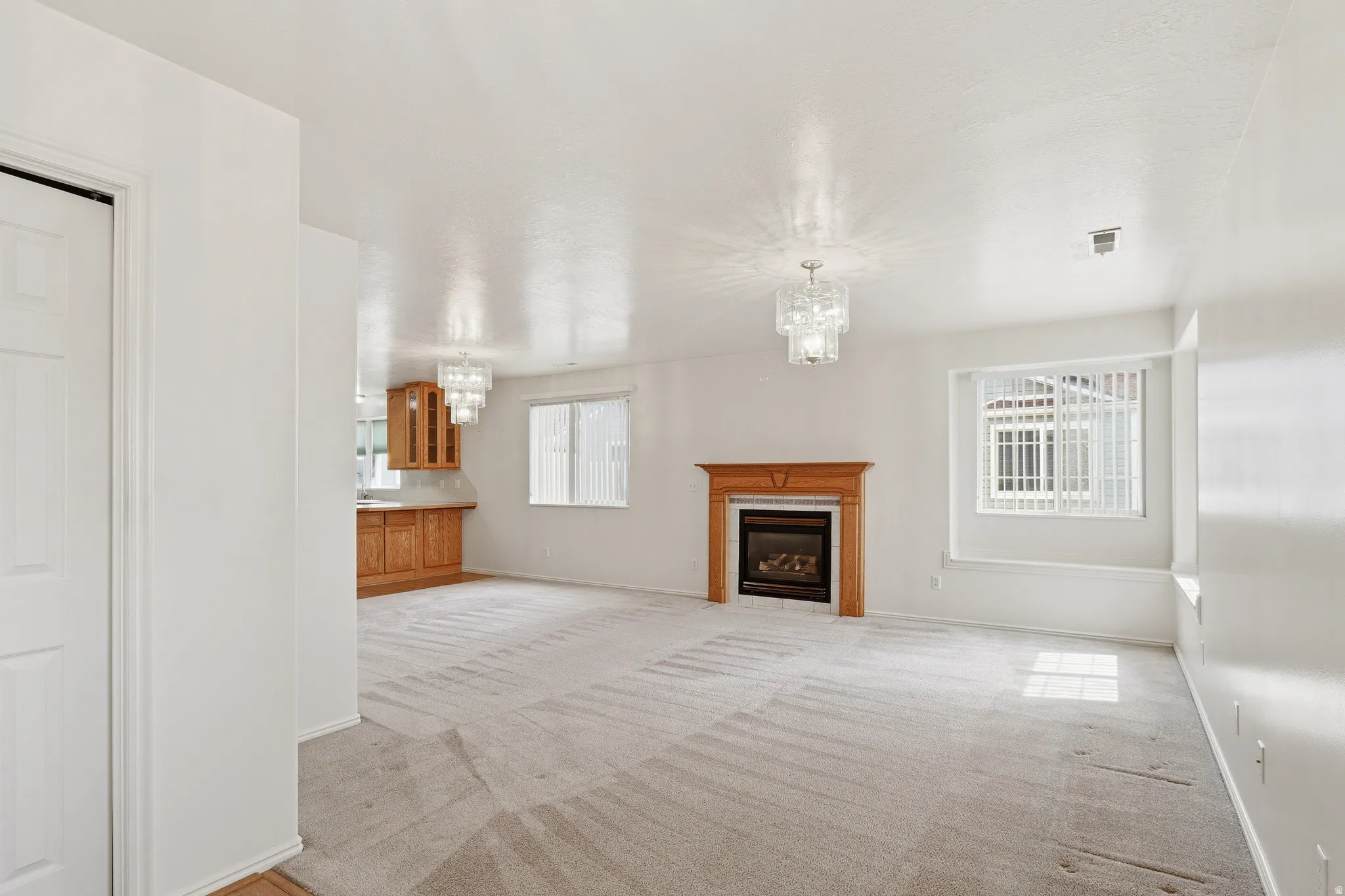 Open-concept living space featuring a fireplace with a wood mantel, light-toned carpeting, and two contemporary light fixtures