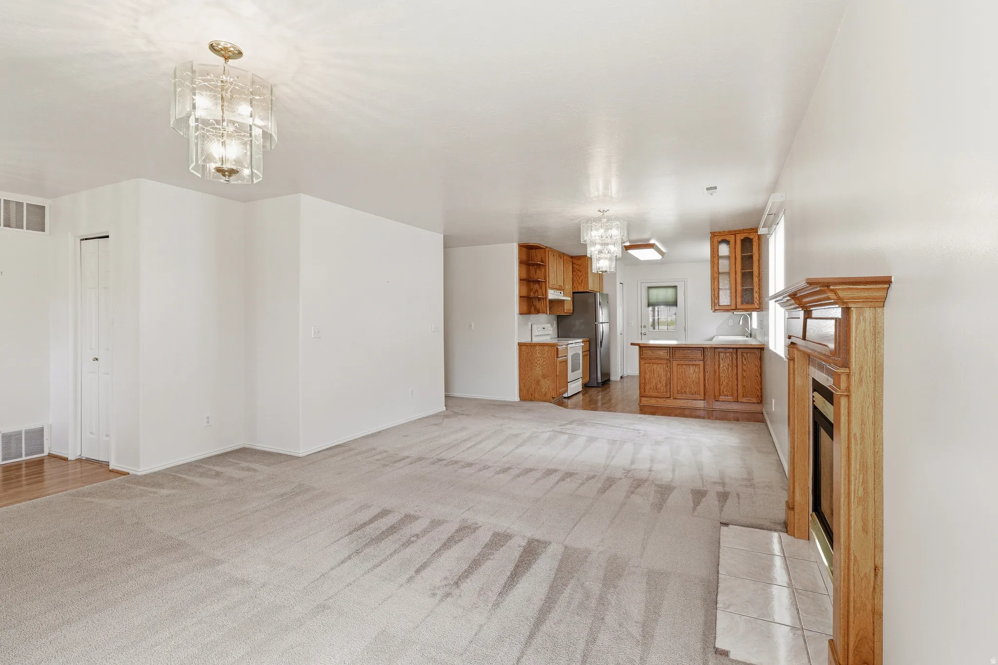 Spacious living area featuring light-toned carpeting and a decorative fireplace with a wood mantel