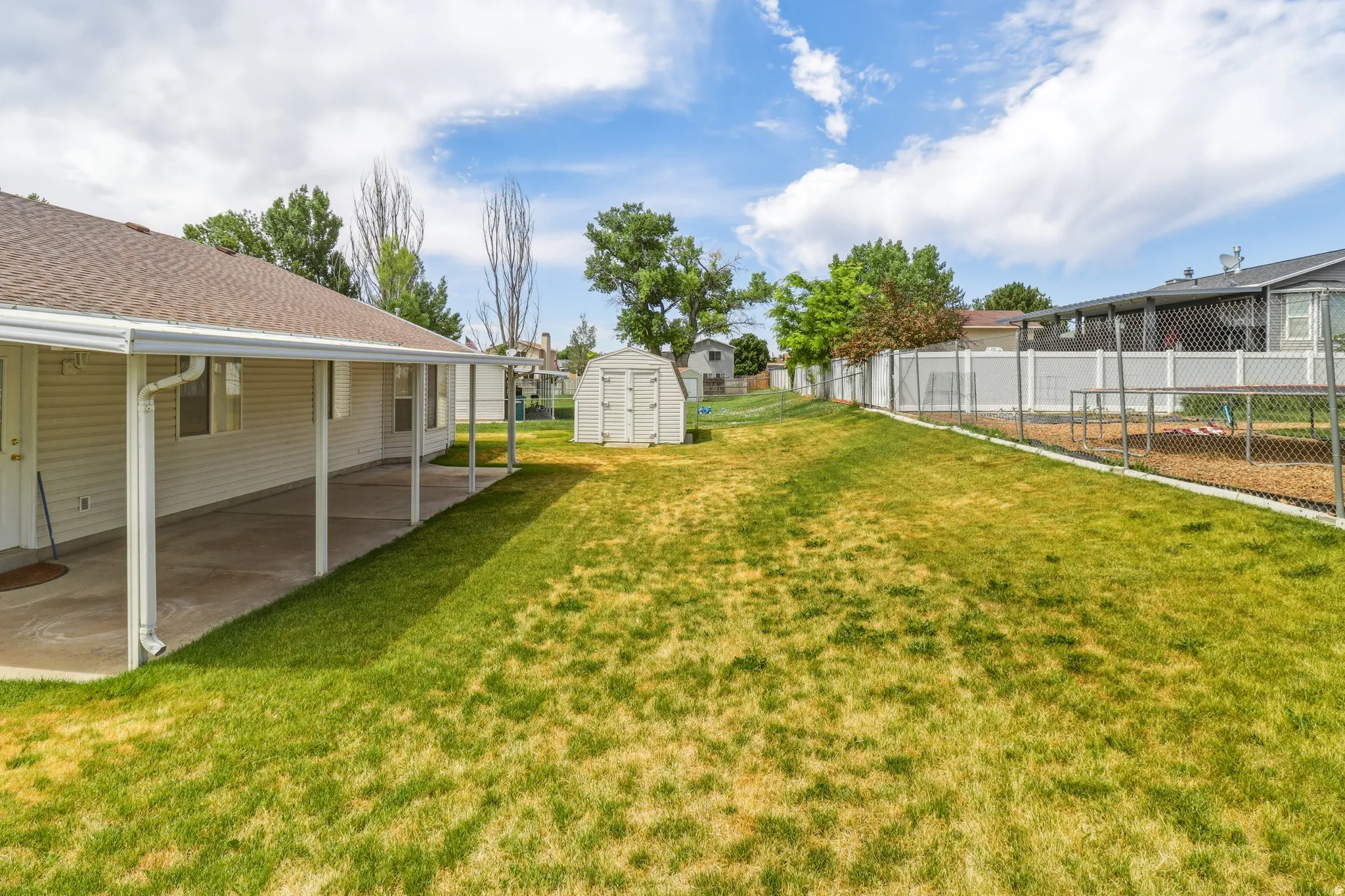 Spacious backyard featuring a covered patio, expansive lawn, storage shed, and perimeter fencing