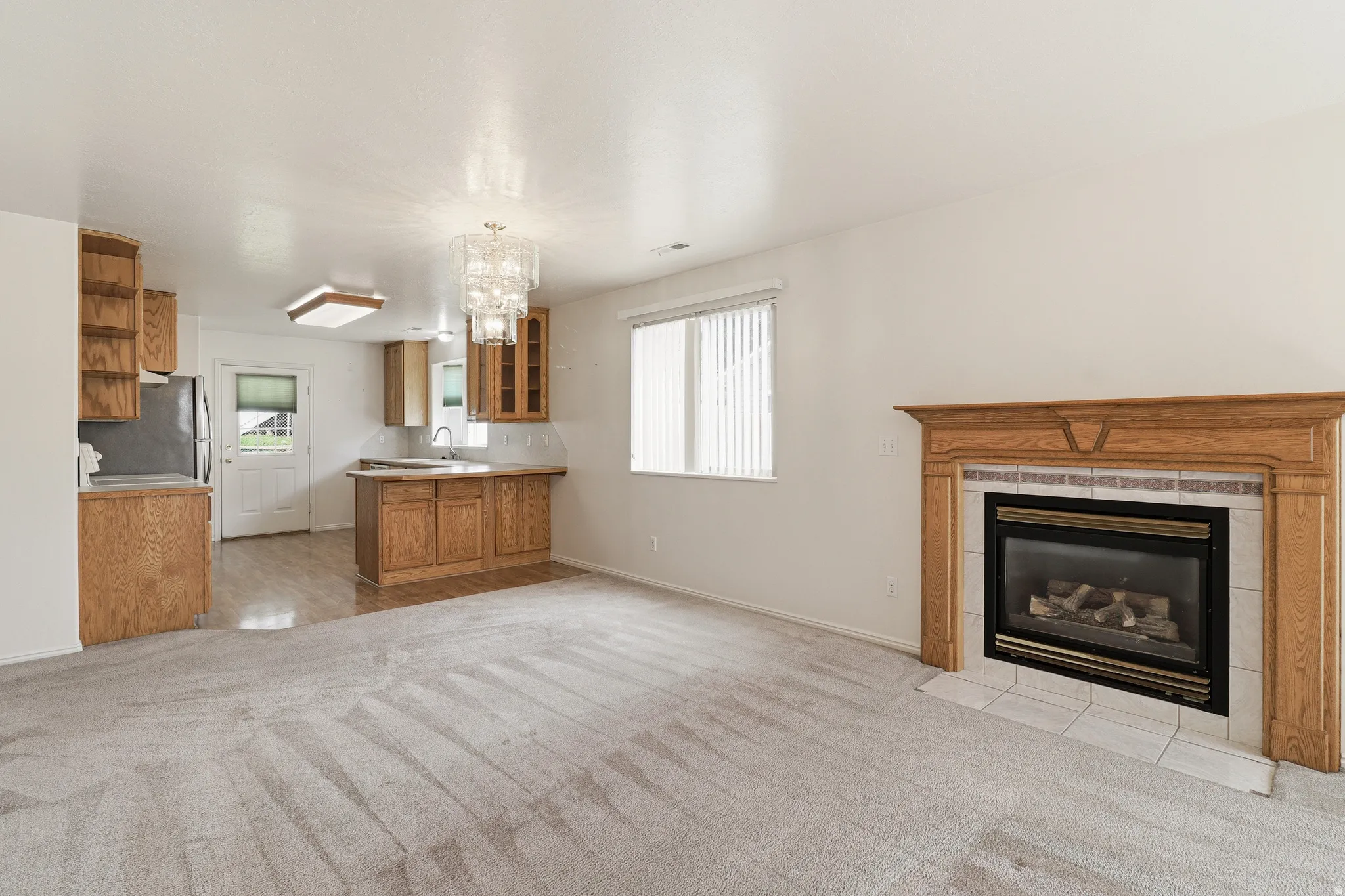 Neutral carpeted area with a gas fireplace featuring a wood mantel