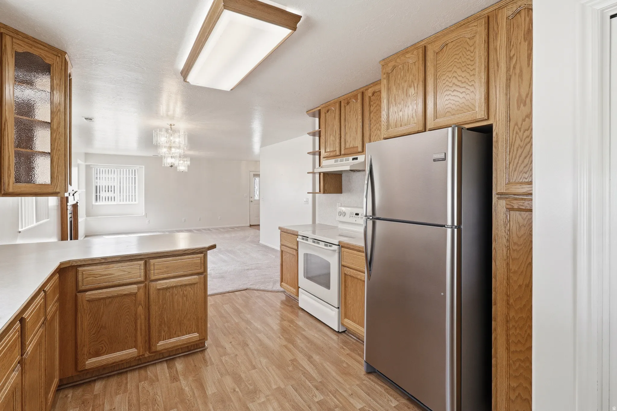 Kitchen featuring light wood cabinetry, laminate countertops, wood-finish flooring, and a full suite of appliances including a stainless steel refrigerator and white range