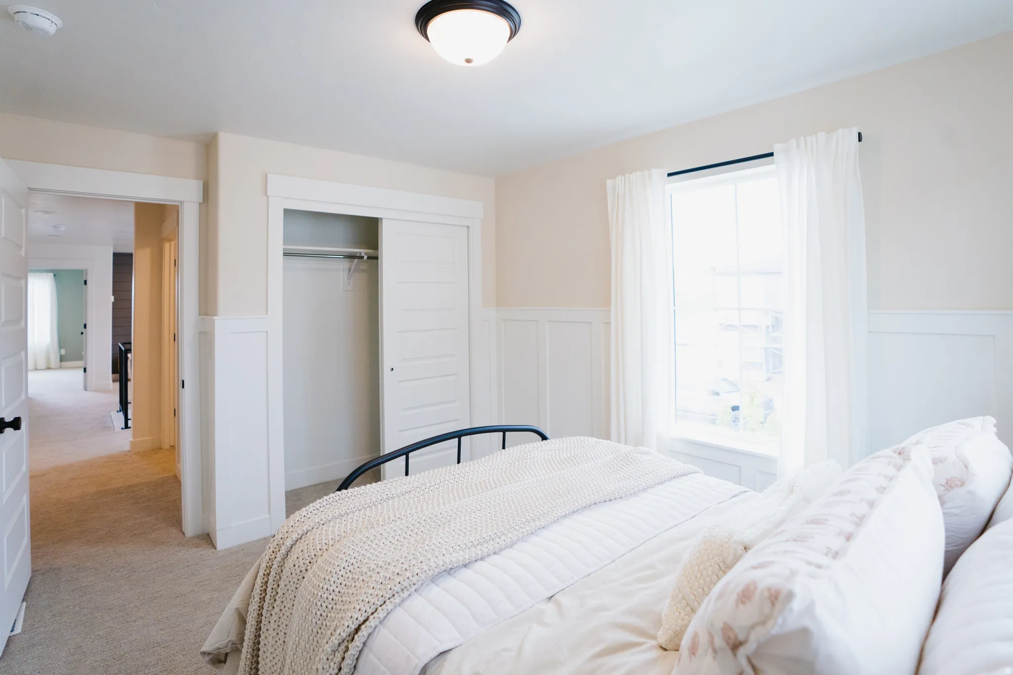 Bedroom featuring light-colored carpet flooring, white wainscoting, an overhead flush-mount light fixture, a window with trim, and a bi-fold closet