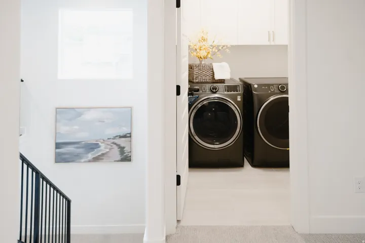 Dedicated laundry area featuring front-loading appliances, white cabinetry, and light-toned tile flooring