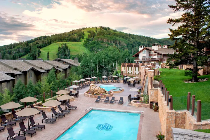 Expansive outdoor amenity space featuring a large swimming pool, a separate hot tub, and multiple lounge areas with umbrellas