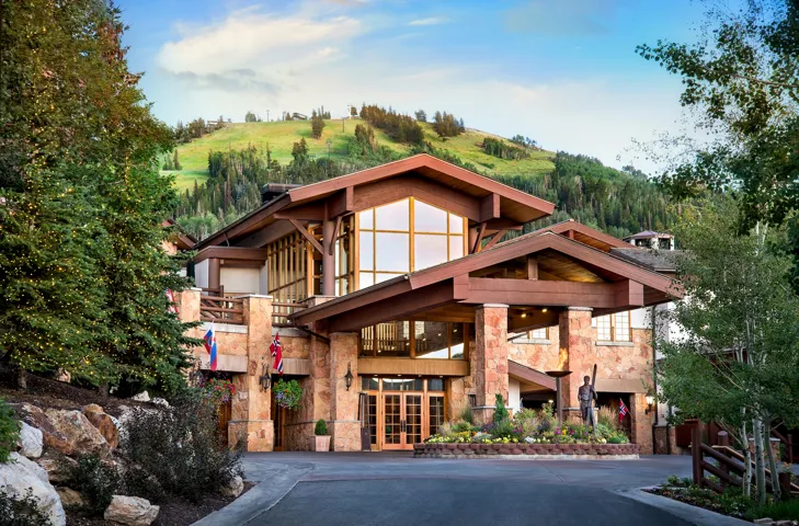 Grand mountain-style lodge entry with a porte-cochere, stone facade, prominent exposed timber beams, and expansive windows