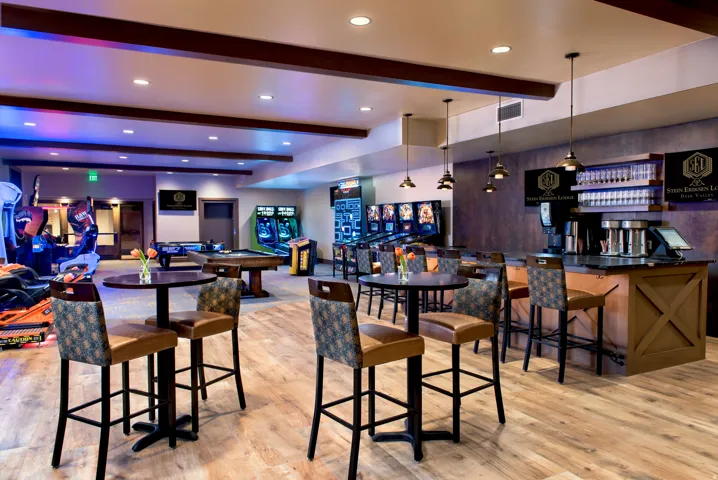 Lounge area featuring wood-finish flooring, a built-in bar with dark countertops, recessed lighting, and exposed ceiling beams