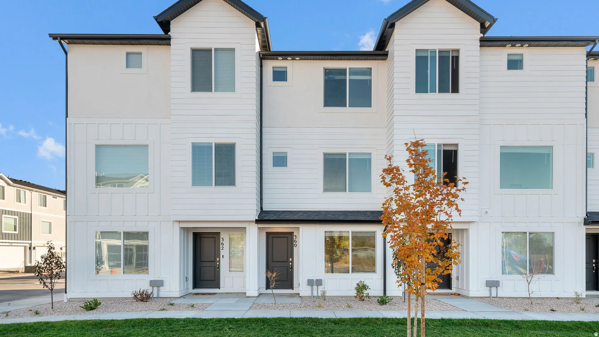 Modern multi-level townhome featuring a clean white facade with contrasting dark trim and a dark roof