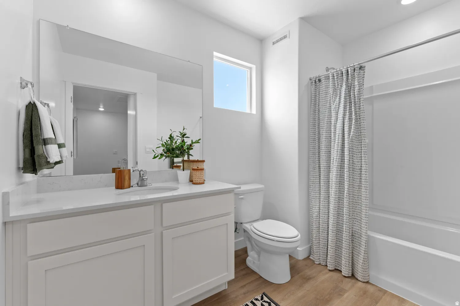 Bathroom featuring a white vanity with a light-toned countertop, a large wall-mounted mirror, a white toilet, and a shower-tub combination