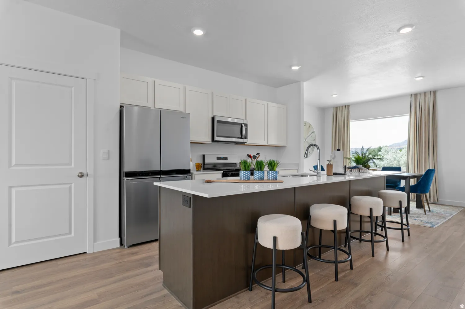 Modern kitchen featuring an expansive center island with seating, stainless steel appliances, white cabinetry, and wood-finish flooring