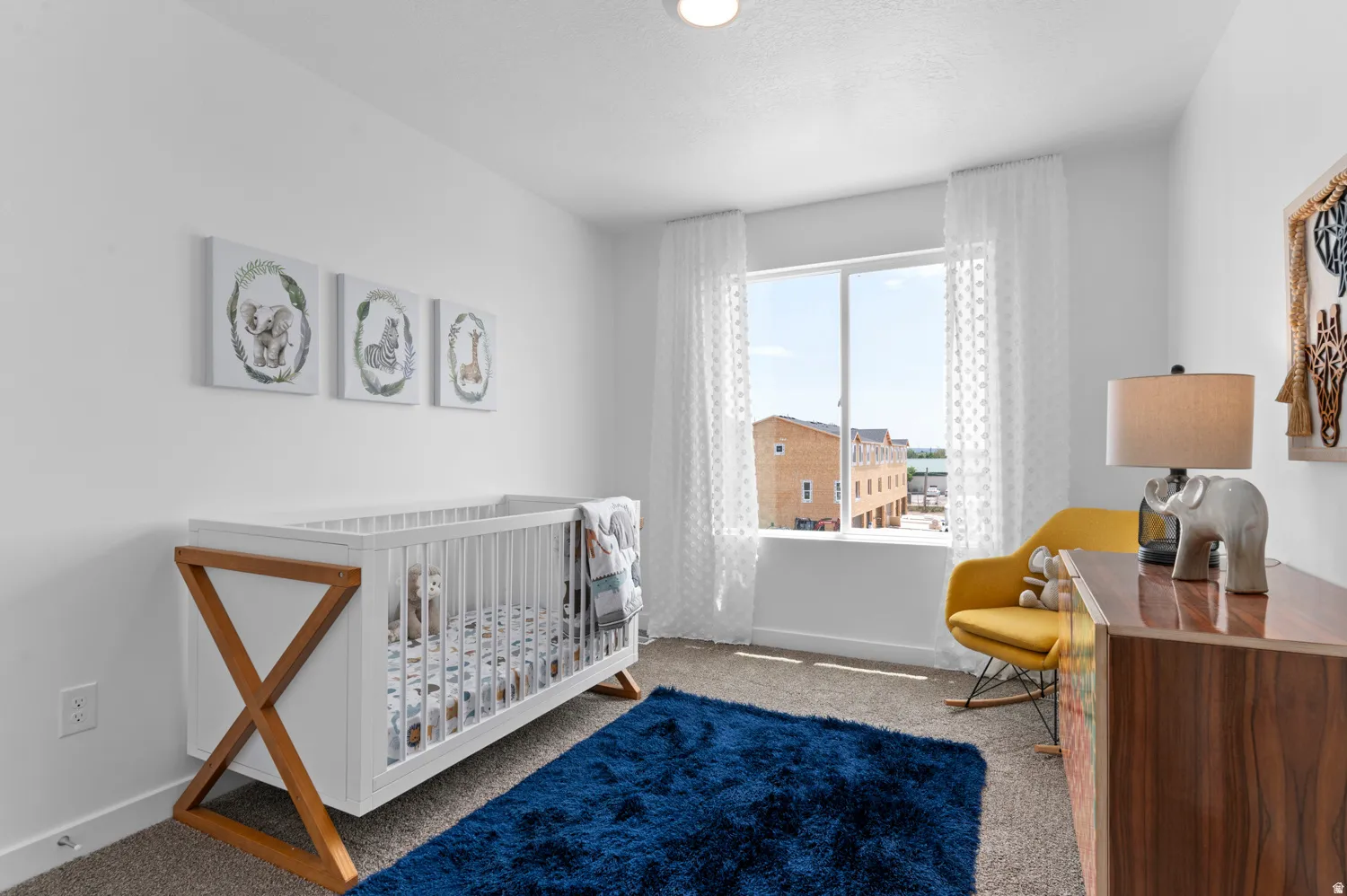 Bright room featuring a large window with white sheer curtains, neutral carpet flooring, and white walls