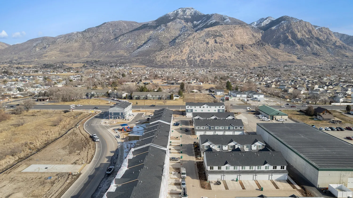 New construction townhome community featuring multiple buildings with dark grey shingle roofs and light-colored siding