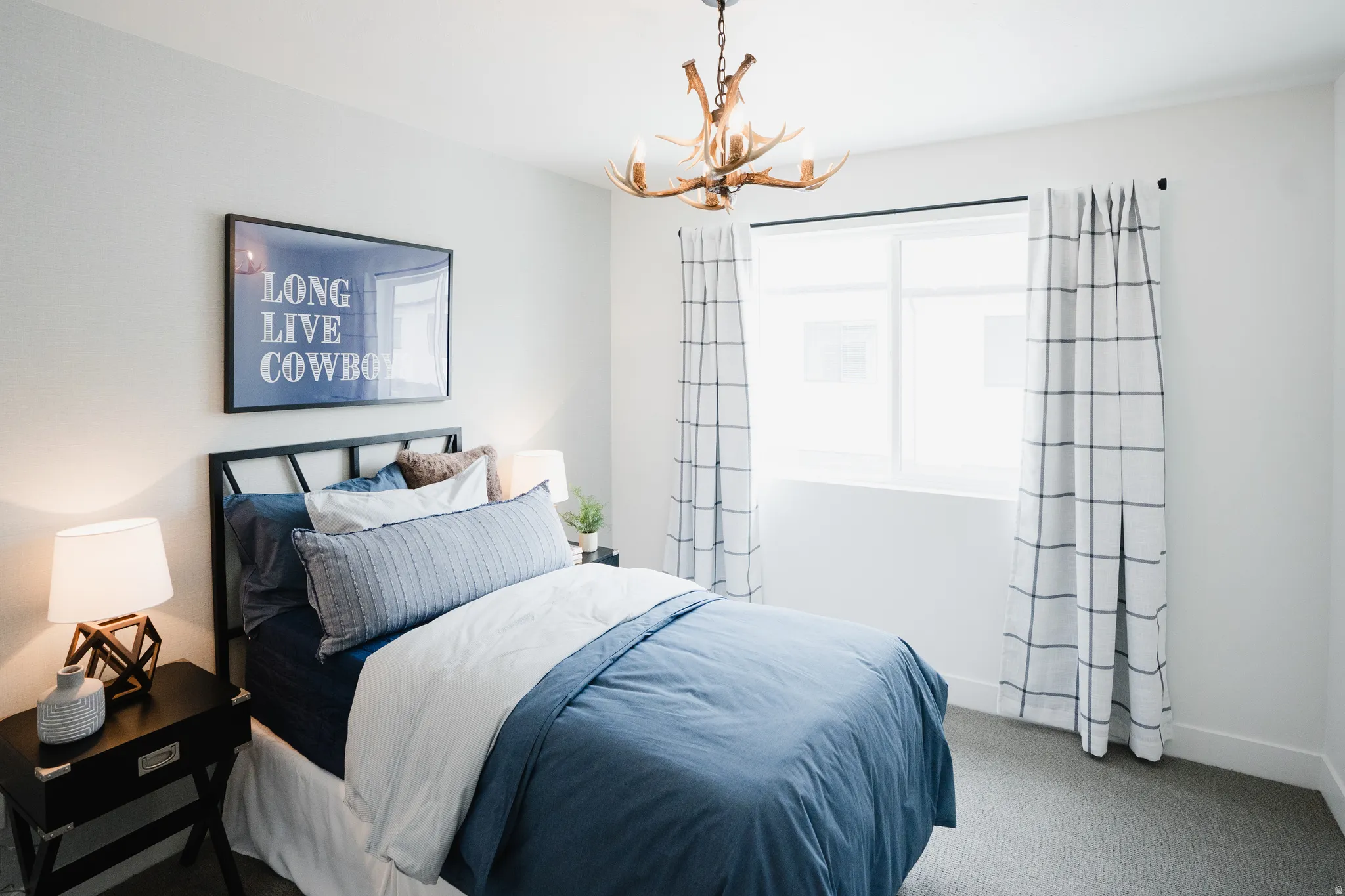 Bedroom featuring a prominent window, antler-style chandelier, and neutral carpet flooring