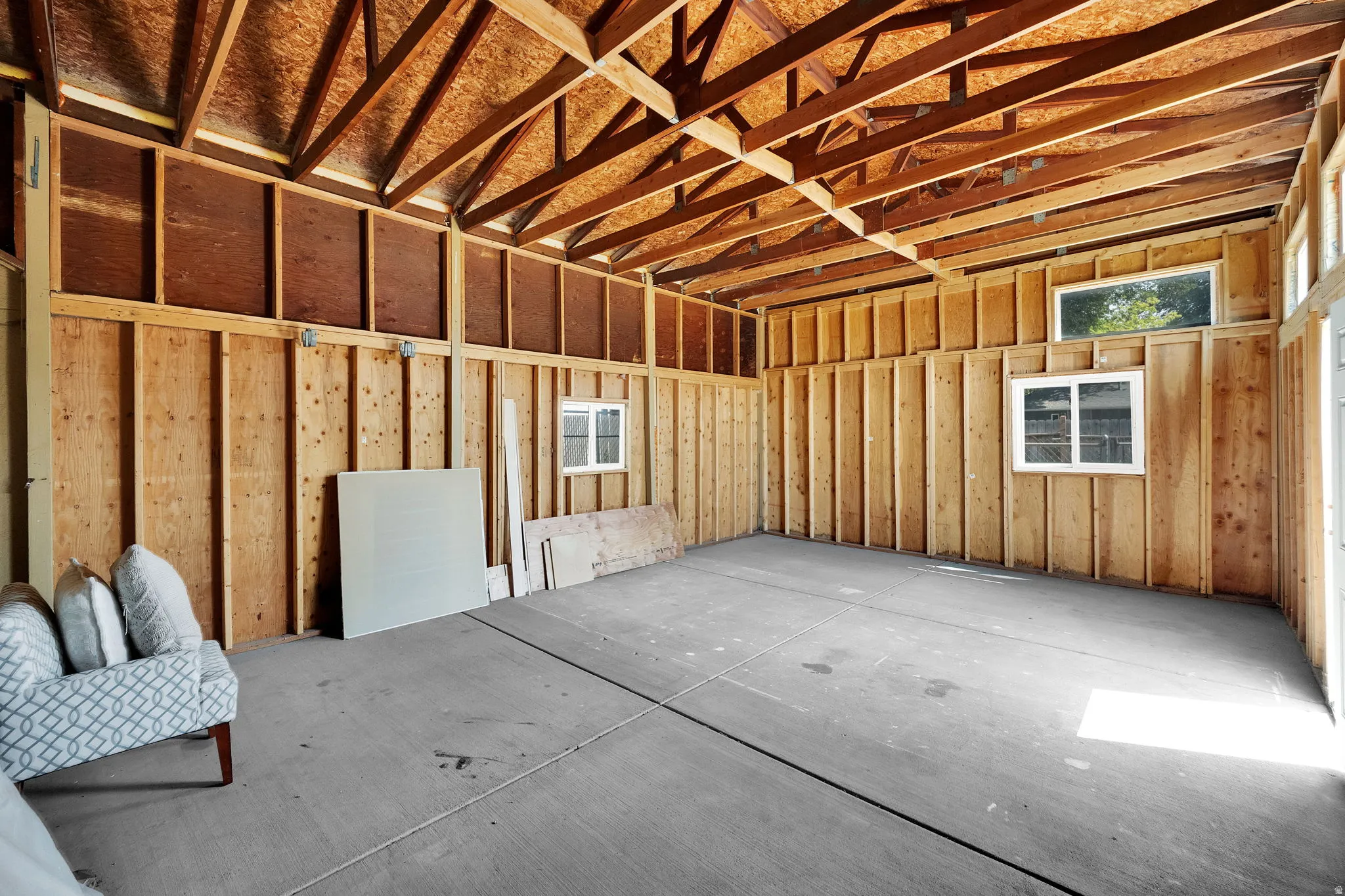 Spacious unfinished room with exposed wood framing, high vaulted ceilings, concrete flooring, and multiple windows providing natural light