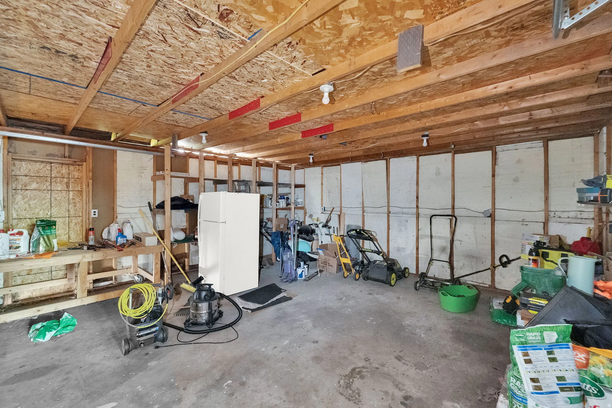 Spacious garage featuring exposed wood framing, concrete flooring, and ample storage shelving