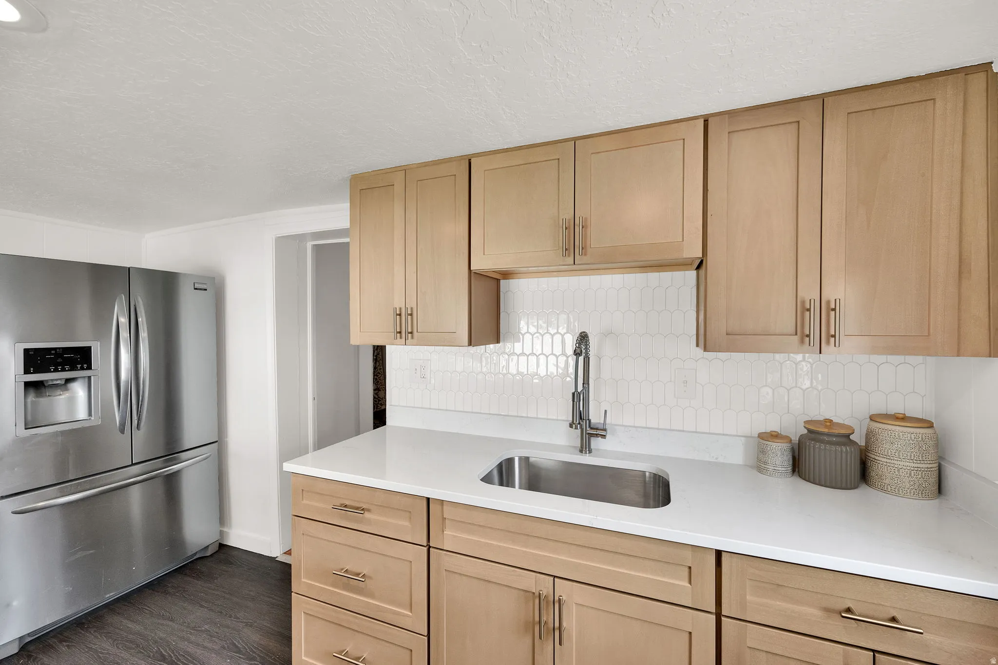 Kitchen featuring light wood-finish cabinetry, white countertops, and a white picket tile backsplash