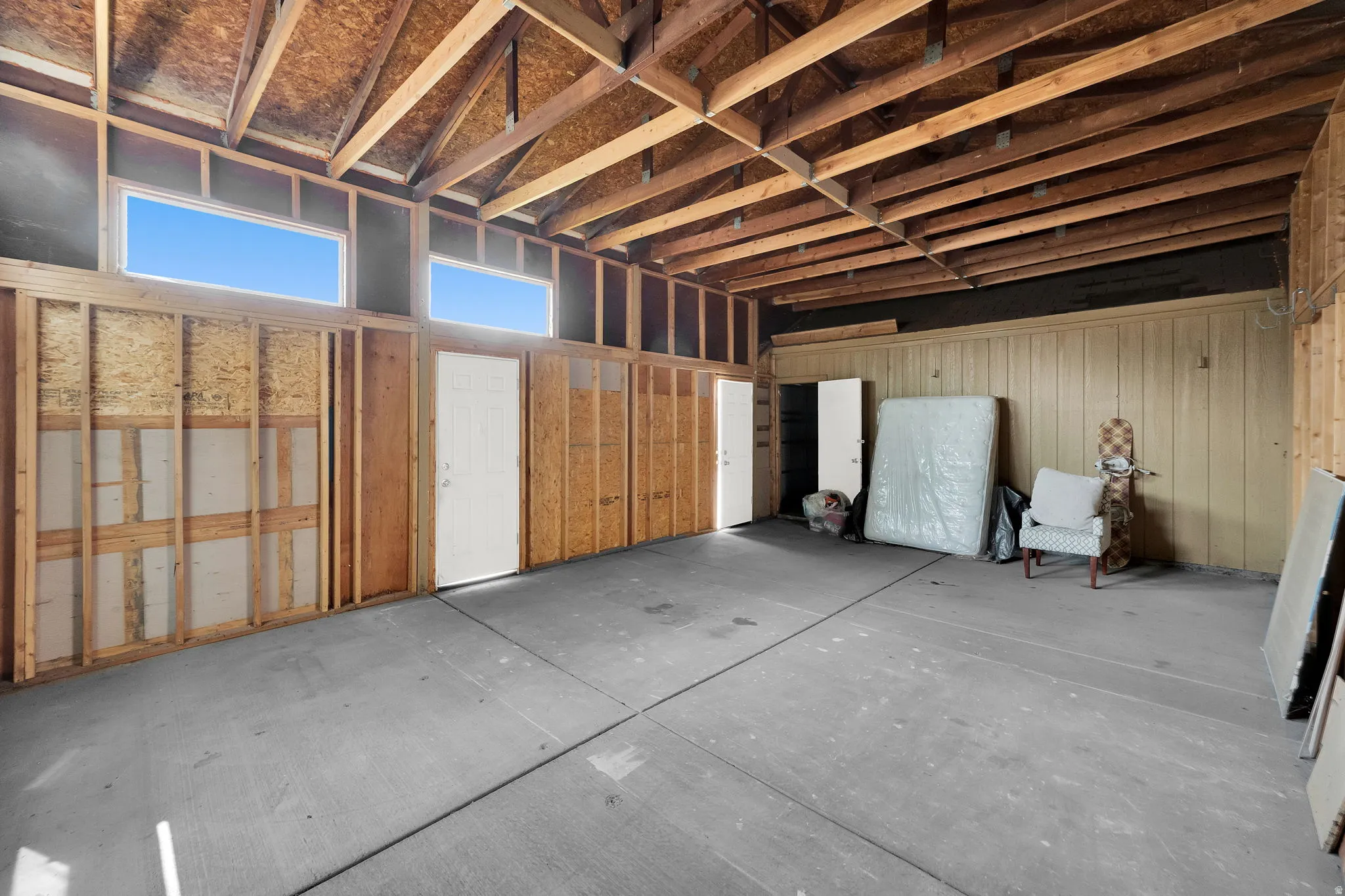 Unfinished interior space featuring exposed wood framing, high ceilings with exposed beams, two transom windows, concrete flooring, and multiple solid panel doors