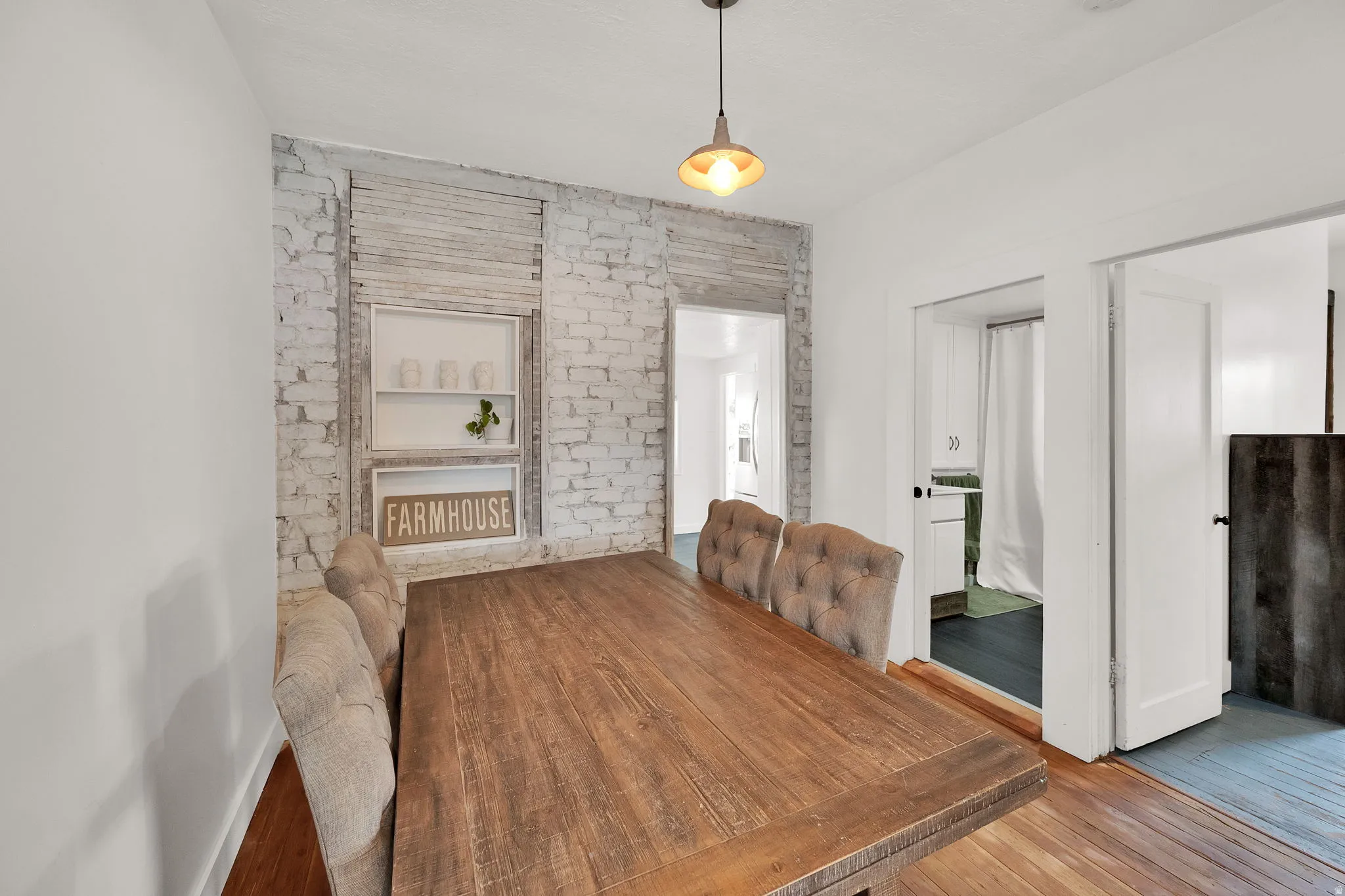 Dining area featuring wood-finish flooring, a white-painted exposed brick wall, and a rustic pendant light fixture
