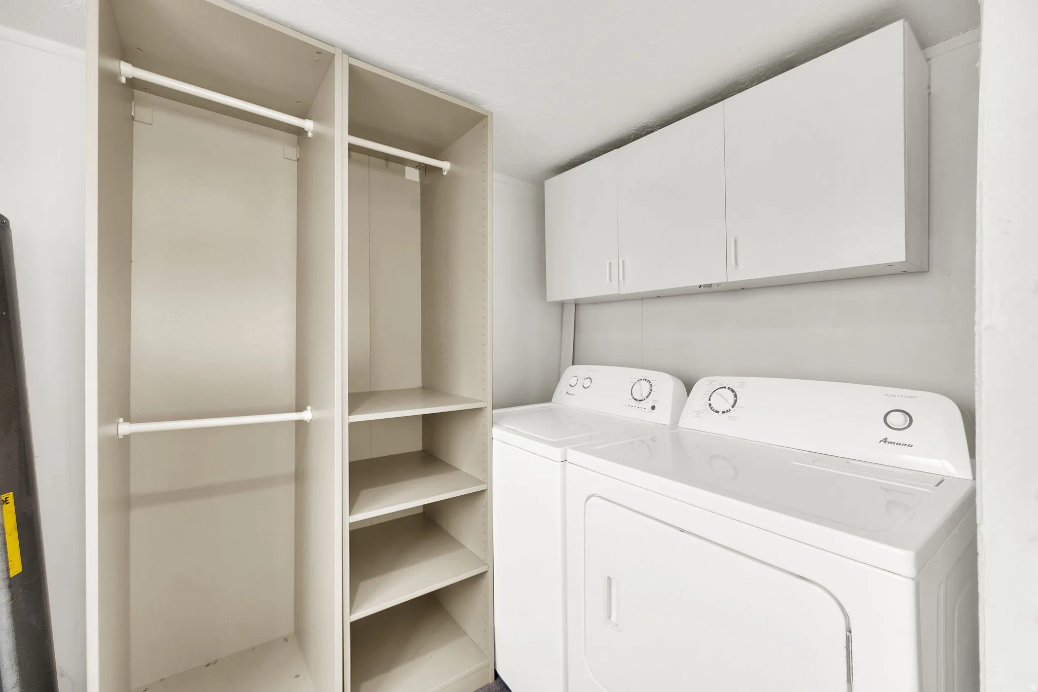 Laundry area featuring a side-by-side washer and dryer, white overhead cabinetry, and a built-in storage system with hanging rods and shelving