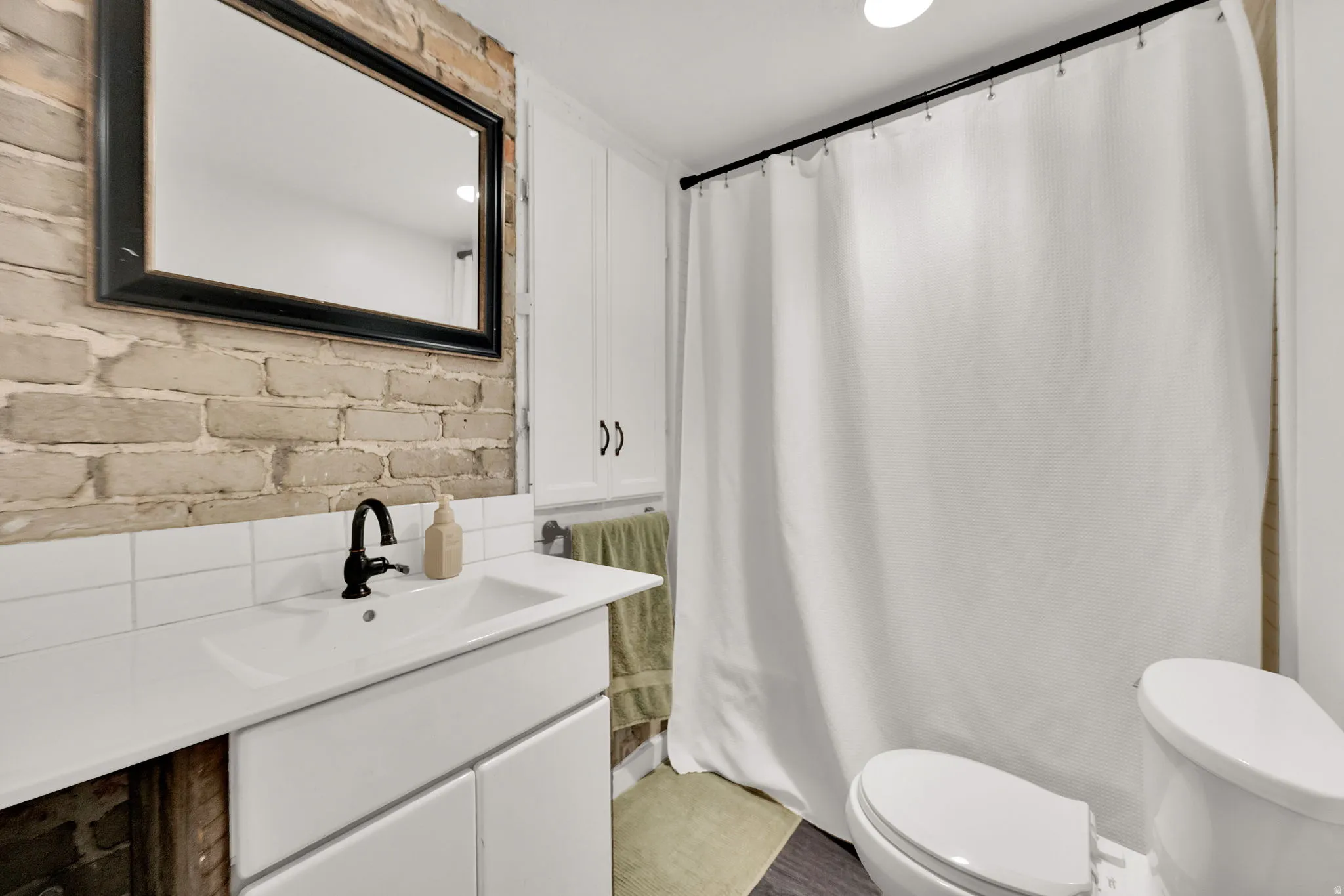 Bathroom featuring an exposed brick accent wall, white vanity with integrated sink, matte black faucet, and white subway tile backsplash