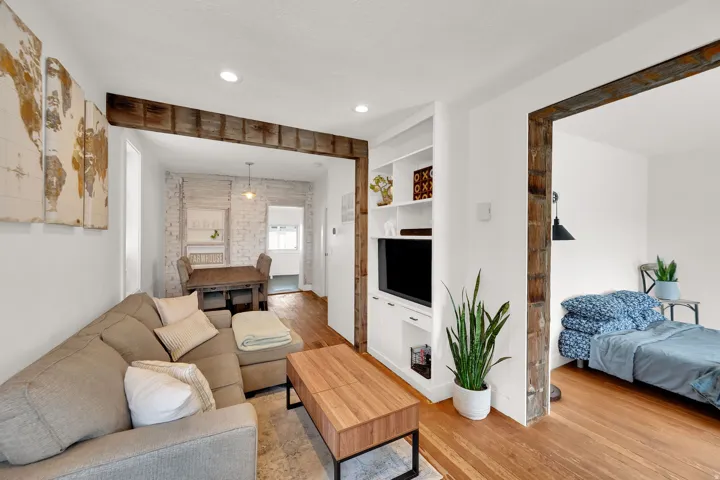 Open-concept living area featuring rich wood-finish flooring, recessed lighting, and exposed beam accents