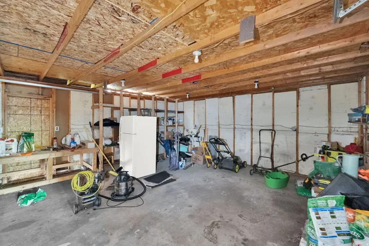 Spacious garage featuring exposed wood framing, concrete flooring, and ample storage shelving